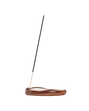 A single incense stick stands upright in a curved, polished brown wooden holder on a plain white background.