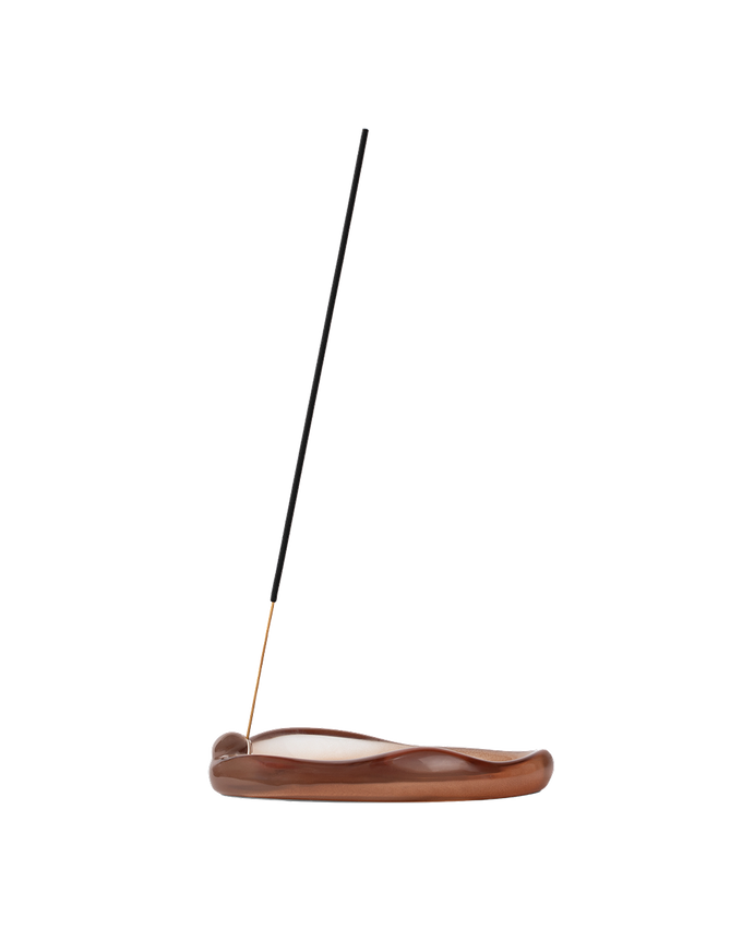 A single incense stick stands upright in a curved, polished brown wooden holder on a plain white background.